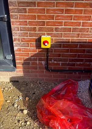 Industrial emergency stop button installed on exterior brick wall, commercial safety works